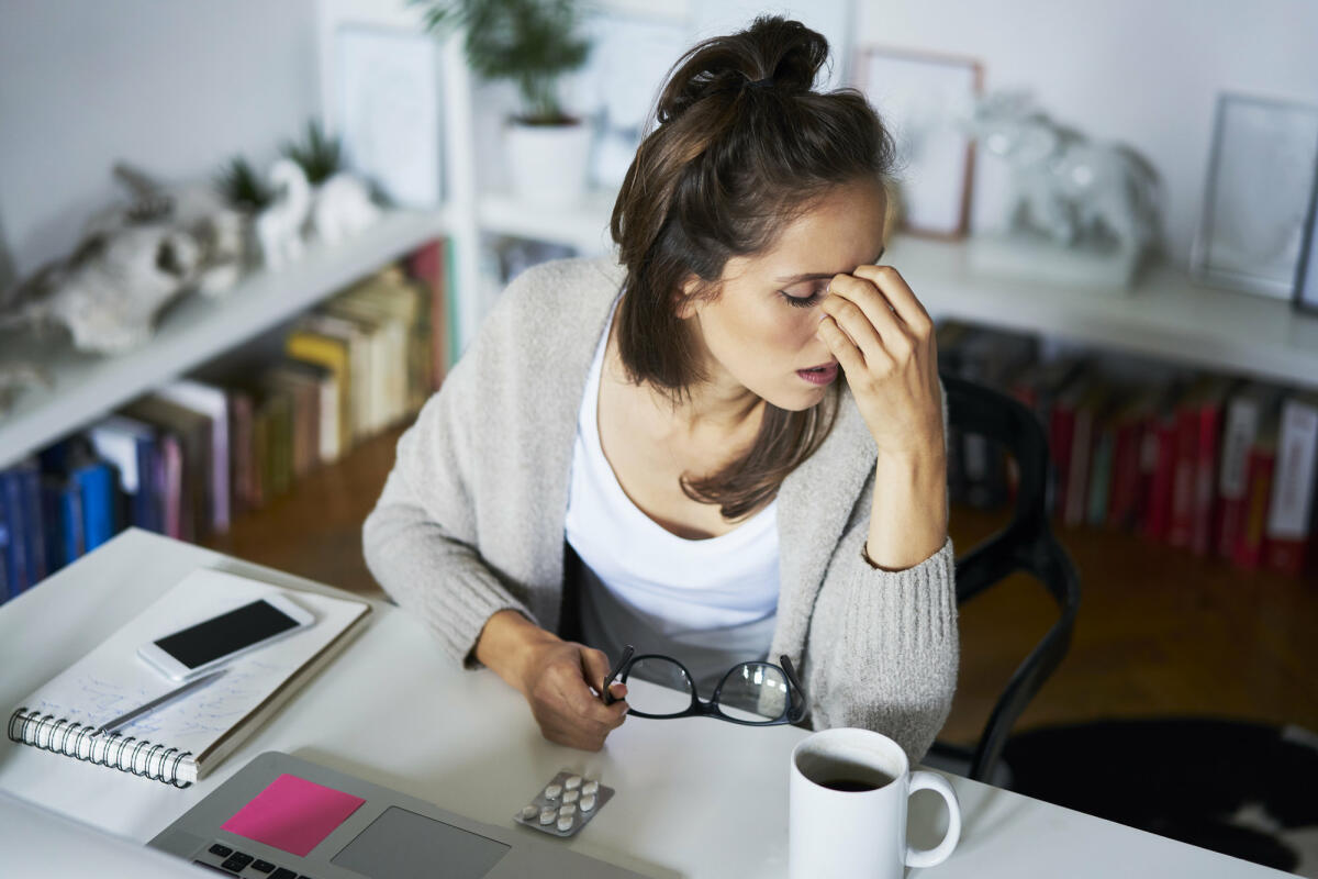 Junge Frau am Schreibtisch mit Kopfschmerzen © Westend61 / Getty Images